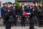 Strażacy idą ze złożoną flagą biało-czerwoną. Z tyłu widoczny marszałek Witold Kozłowski.