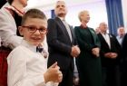 Uśmiechnięty chłopczyk w białej koszuli i okularach. W tle - Iwona Gibas z zarządu województwa oraz radny Rafał Stuglik
