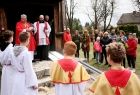 Dwaj kapłani i wierni z palmami wielkanocnymi przed zabytkowym, drewnianym kościołem