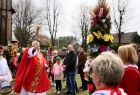 Ksiądz skrapiający kropidłem przed kościołem palmy wielkanocne i uczestników nabożeństwa 