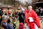 Kapłan święcący kropidłem palmy wielkanocne trzymane przez dzieci