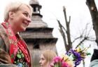 Iwona Gibas z zarządu województwa trzymająca wielkanocną palmę. W tle drewniana wieża zabytkowego kościoła
