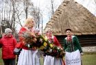 Panie w strojach ludowych z wielkanocną palmą przed chatą krytą strzechą