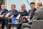 Wicemarszałek Łukasz Smółka słucha patrzy na prowadzącego. Obok siedzą prelegenci.