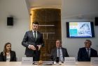 Wicemarszałek Łukasz Smółka stoi przy stole i przemawia. Obok siedzą pozostali uczestnicy wydarzenia.