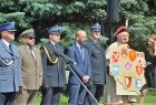 Przedstawiciele służb mundurowych stoją na trybunie honorowej. Z tyłu widoczna zieleń.