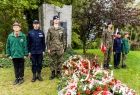 Uczniowie szkół ze szkół mundurowych stoją obok pomnika. Na pierwszym planie kwiaty.