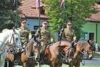 Żołnierze na koniach. Z tyłu widoczna zieleń i budynki.