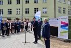 Przemawia do zgromadzonych ludzi wicemarszałek. W tle widoczny szpital.
