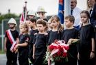 Dzieci trzymają wiązankę kwiatów przepasaną flagą białą-czerwoną.
