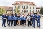 Grupa uczestników wydarzenia w Wieliczce trzyma symboliczne czeki na inwestycje