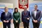 Zdjęcie grupowe. Marszałek, wójt, dyrekcja i kierownictwo ZDW. W tle godło, logo Małopolska oraz fundusze europejskie. 