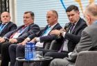 Wicemarszałek Łukasz Smółka trzyma mikrofon i przemawia. Obok siedzą prowadzący debatę i prelegenci.