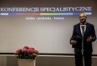 Mężczyzna przemawia na scenie. Za nim napis Konferencje Specjalistyczne.