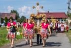 Mieszkańcy w barwnych strojach niosą wieniec dożynkowy