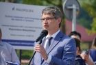 Wójt gminy Tymbark Paweł Ptaszek stoi przed mikrofonem. W tle widać białą tablice informująca o funduszach europejskich pozyskanych na budowę miasteczka rowerowego. 