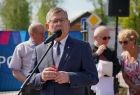 Marszałek Witold Kozłowski stoi przy mikrofonie, za nim widać kilka osób, w tle na płocie zawieszony jest niebieski baner z napisem Małopolska i logiem województwa.