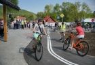 Dwójka dzieci na rowerach pokonuje łuk alejki. Na drodze namalowano białe linie informujące o zakazie wyprzedzania. W tle widać innych rowerzystów i pieszych korzystających z chodnika. Przy drodze znajduję się znak z pierwszeństwem przejazd.