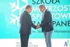 Marszałek Województwa Małopolskiego Witold Kozłowski gratuluję mężczyźnie. Wszyscy stoją na scenie, w tle widać niebieską planszę i fragment kolorowego loga województwa Małopolskiego. 