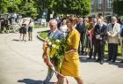 Marta Malec-Lech z zarządu województwa składa wieniec przed pomnikiem. Obok idzie mężczyzna.