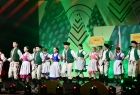 Dziewczęta i chłopcy w strojach regionalnych podczas tańca, w tle zielone dekoracje