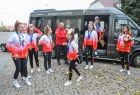 Grupa cheerleaderek wychodzi z czarnego samochodu na podwórze, dziewczyny maja na sobie bluzy w białoczerwonych kolorach. W tle widać zabudowania i zielone drzewa. 