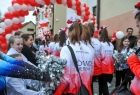 Zawodniczki w białoczerwonych bluzach przechodzą przez bramę z białoczerwonych balonów, dziewczyny ustawione są tyłem do zdjęcia wokoło widać dzieci i witających je kibiców. 