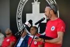 prezes Sądeckiego WOPR podczas wystąpienia, za nim siedzą na ławce ubrani w czerwone koszulki ratownicy WOPR