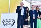 Marszałek Witold Kozłowski stoi w otoczeniu organizatorów i hostess stojących na scenie w prawym dolnym rogu widać biała plansze z kołami olimpijskimi. 