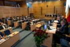 Widok na sale sejmiku województwa małopolskiego z prawej strony widać członków prezydium rady z lewej radnych sejmiku. W sali dominuję brązowy kolor ścian. Z lewej strony za prezydium widać, flagę małopolski. 