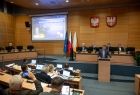Widok na sale sejmiku województwa małopolskiego, na wprost widać siedzących przy biurku członków prezydium. Z lewej członków zarządu województwa małopolskiego, na pierwszym planie widać siedzących tyłem do zdjęcia radnych. 