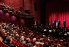 Widok na wnętrze Opery Krakowskiej wypełnionej ludźmi. Wewnątrz dominują ciemno czerwone kolory. 