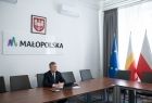 Marszałek Witold Kozłowski podczas spotkania online z szefem administracji Obwodu Lwowskiego Maksym Kozicki. Na ścianę widać napis Małopolska i logo w Kształcie litery M. Z lewej strony widać flagi Polską, Małopolską i Unijną.