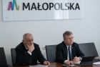 Marszałek Witold Kozłowski i Jan Tadeusz Duda na spotkaniu online z szefem administracji Obwodu Lwowskiego Maksym Kozicki. Na ścianę widać napis Małopolska i logo w Kształcie litery M. Z lewej strony widać flagi Polską, Małopolską i Unijną.