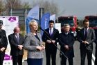 Iwona Gibas przemawia podczas wydarzenia. Z tyłu widoczni ludzie i wozy strażackie.