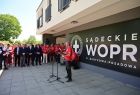 prezes Sądeckiego WOPR podczas wystąpienia, za nim siedzą na ławce ubrani w czerwone koszulki ratownicy WOPR