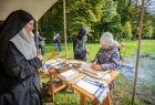 Kobieta z grupy rekonstrukcyjnej w stroju historycznym stoi przy stoisku. 