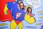 Ojciec i córka, których głowy widać na tle komiksowej sylwetki supermena trzymającego w ręku małe dziecko