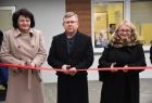 Radna wojewódzka Jadwiga Wójtowicz, marszałek małopolski Witold Kozłowski, wójt gminy Sękowa Małgorzat Małuch, przecinają czerwoną wstęgę przy wejściu do nowego przedszkola w Sękowej. W tyle widać elewację budynku i okna przedszkola.