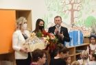Pracownicy Przedszkola, przekazują podziękowania marszałkowi Witoldowi Kozłowskiemu. Przedszkolanki trzyma w ręku kwiaty i skrzynkę z miodami. W tle widać kolorowe szafki i ścianę pokryta kolorowymi rysunkami z motywami roślinnymi. 
