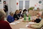 Marszałek Witold Kozłowski, radna Jadwiga Wójtowicz, wójt gminy Sękowa Małgorzata Małuch. Spotkanie w domu Seniora w Męcinie Wielkiej. Grupa seniorek siedzi wspólnie z marszałkiem przy stole, przed nimi ułożone są kartki z tekstem kolęd.