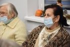 Spotkanie w domu seniora w Męcinie Wielkiej. Na pierwszym planie widać dwie Seniorki, w trakcie wspólnego Kolędowania. W tle parapet na którym położono ręcznie wykonane stroiki świąteczne. 