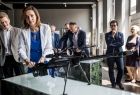 Marta Malec-Lech z zarządu województwa z pozostałymi uczestnikami spotkania podczas zwiedzania hali produkcyjnej ogląda karabin.