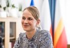 Kobieta siedzi na tle flag Polski i MAłopolski. 