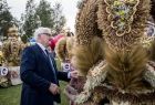 Wicemarszałek Józef Gawron, stoi przy wieńcu dożynkowym. Wieniec wykonany jest ze zboża i kwiatów. W tle widać , kilka innych wieńców dożynkowych, zielone drzewa i zachmurzone niebo. 