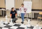 Dziewczynka gra w ogromne szachy z pomocą osoby dorosłej