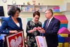 Marszałek Małopolski Witold Kozłowski, radna Jadwiga Wójtowicz i dyrektor szkoły stoją obok siebie wewnątrz klasy. Radna Jadwiga Wójtowicz trzyma w ręku godło Polski. 