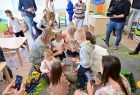 Przedszkolaki i opiekunowie, siedzą na kolorowym dywanie, dzieci bawią się zabawkami. 