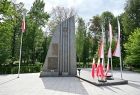 Widok na grybowski Pomnik poległych w II wojnie światowej. postument z pewnej odległości po prawej flagi