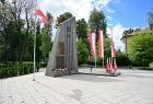 Widok na grybowski Pomnik poległych w II wojnie światowej. postument z pewnej odległości po prawej flagi